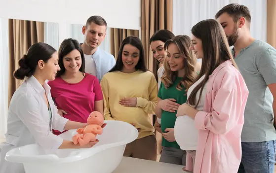 Hebamme mit Babypuppe und Menschen außenherum